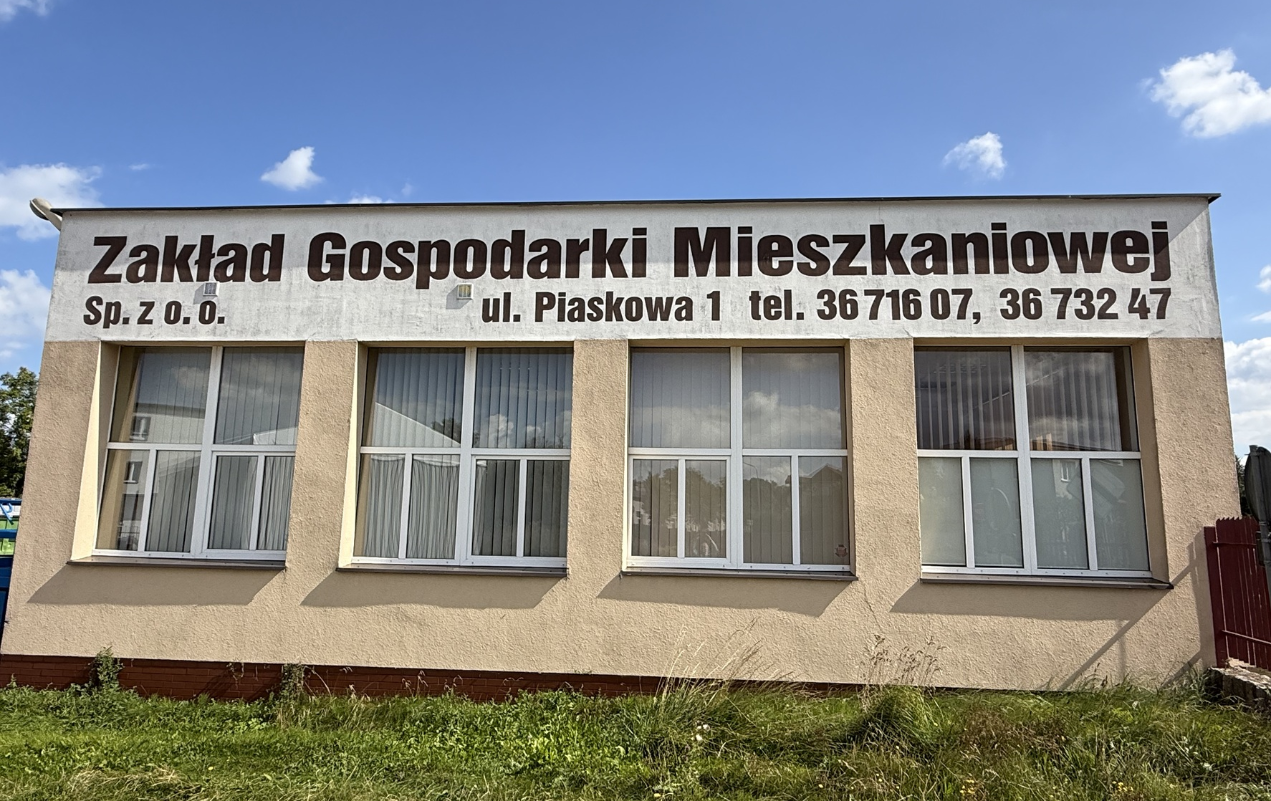 ZGM Budynek z zewnątrz na namalowaną nazwą spółki i jej adresem oraz numerem kontaktowym na telefon.